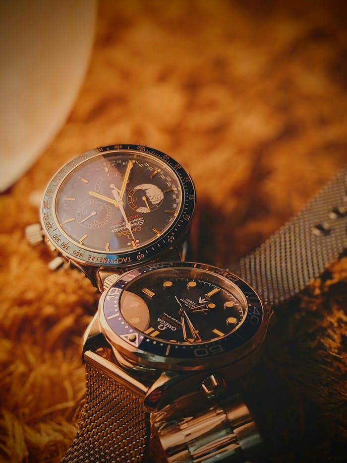 Close-up of two luxury watches with metal straps on a soft textured surface, showcasing timeless elegance.